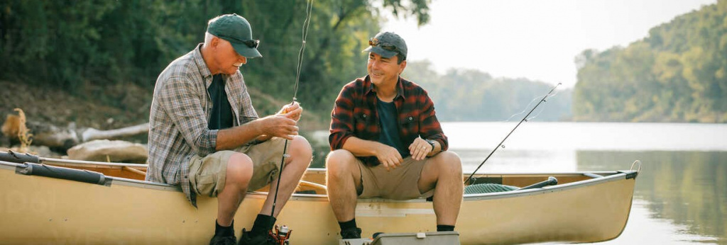friends-with-fishing-rods-talking-while-sitting-on-boat-at-lakeshore-CAVF59020.jpg
